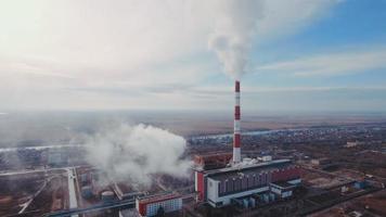 Aerial shot. Pipes with smoke industrial production, plant, air pollution. Dense thick smoke comes from industrial red white pipes from a bird's eye view. Industrial zone smoke comes from the pipe