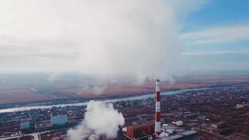 Aerial shot. Pipes with smoke industrial production, plant, air pollution. Dense thick smoke comes from industrial red white pipes from a bird's eye view. Industrial zone smoke comes from the pipe