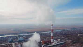 Aerial shot. Pipes with smoke industrial production, plant, air pollution. Dense thick smoke comes from industrial red white pipes from a bird's eye view. Industrial zone smoke comes from the pipe video