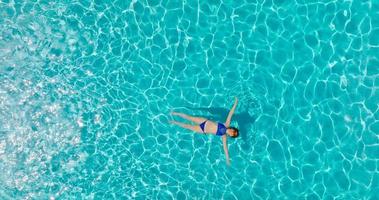 topo baixa Visão do uma mulher dentro uma azul roupa de banho deitado em dela costas dentro a piscina. video