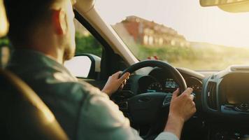 Mens schijven een auto langs de weg, de instelling zon schijnt in de voorruit. video