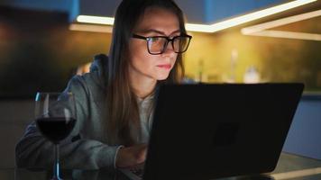 Woman is sitting in the kitchen and working on a laptop at night video