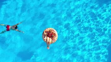 couple ayant amusement dans le piscine, le homme nage et le femme mensonges sur une Donut video