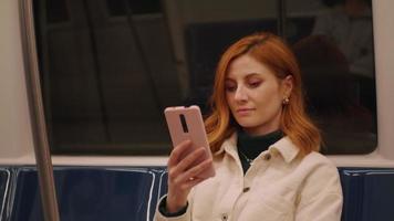 vrouw browsen sociaal media nieuws, glimlachen terwijl lezing Aan smartphone scherm in openbaar vervoer. video