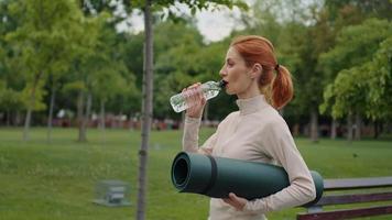Woman drinking water after fitness training in the park, side view video
