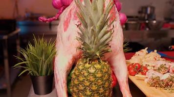 Full size raw lamb meat on table with knife in it and pineapple for decor. video