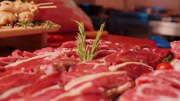 uppsättning av rå nötkött biffar och utegrill grillspett dekorerad med rosmarin och tomater. video