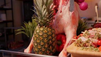 Close up full size raw lamb meat on table with knife in it and pineapple for decor. video