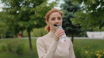 caucásico mujer Bebiendo agua desde botella después al aire libre ejercicio. video