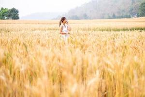 joven asiático mujer en blanco vestidos caminando en el cebada arroz campo foto