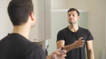 The man is spraying perfume. Handsome young man looking at himself in the mirror is spraying perfume to smell good. video