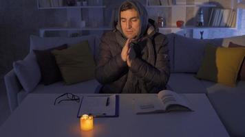 Power cut. Man trying to warm himself with candles out of desperation in the cold at home. video