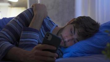 das Mann suchen beim das Telefon beim Nacht ist dösen im seine Bett. schläfrig jung Mann suchen beim Telefon stattdessen von gehen zu Bett und betäubt. video