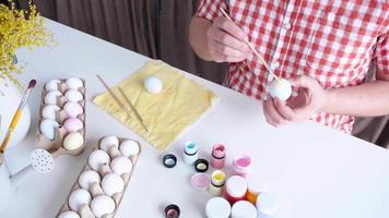 Young man coloring eggs sitting at the kitchen at home video