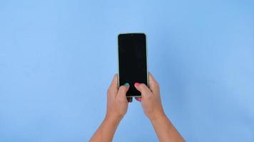 vrouw hand- Holding de smartphone Aan pastel blauw achtergrond in studio. mobiel telefoon mock-up voor uw Product. video