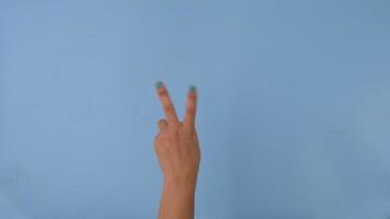 hembra mano demostración gesto de paz en pastel azul pantalla antecedentes. paquete de gestos movimientos y cuerpo idioma. video