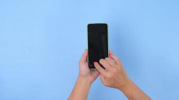 donna mano Tenere il smartphone su pastello blu sfondo nel studio. mobile Telefono modello per il tuo Prodotto. video