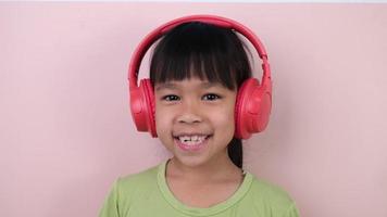 süß wenig Mädchen im Kopfhörer Hör mal zu zu Musik. kabellos Headset Gerät Zubehörteil. Kind genießen Musik- im Kopfhörer auf Pastell- Rosa Hintergrund im Studio. video