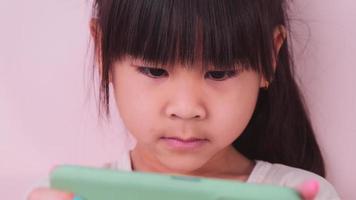 Cute little girl holding smartphone enjoying using mobile app playing games at home. Little Asian girl studying on mobile phone, watching video. Child and technology concept. video