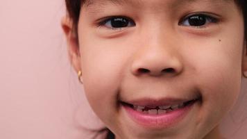 linda pequeño niña sonriente felizmente blanco dientes. de cerca de joven hermosa sonriente niña demostración su dientes aislado en rosado antecedentes. concepto de bueno salud en infancia. video