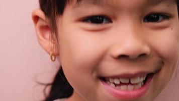 linda pequeño niña sonriente felizmente blanco dientes. de cerca de joven hermosa sonriente niña demostración su dientes aislado en rosado antecedentes. concepto de bueno salud en infancia. video