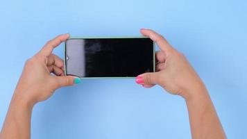 vrouw hand- Holding de smartphone Aan pastel blauw achtergrond in studio. mobiel telefoon mock-up voor uw Product. video