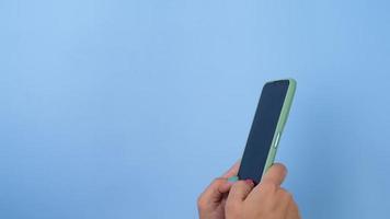 Woman hand holding the smartphone on pastel blue background in studio. Mobile phone mock-up for your product. video