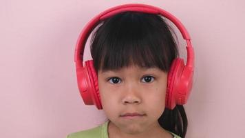 linda pequeño niña en auriculares escucha a música. inalámbrico auriculares dispositivo accesorio. niño disfrutando música en auriculares en pastel rosado antecedentes en estudio.