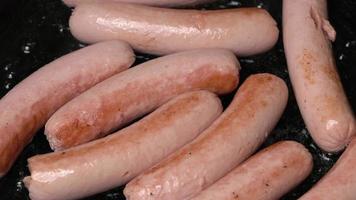 Close up of meat bratwurst fried in black pan with oil. Close-up view of cooking of delicious, high-calorie non-vegetarian junk food with large content of cholesterol video