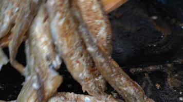 Cooking frying and stirring capelin fish fried in iron pan. Close-up view of chef stirs roasted caplin fish with wooden spatula. Grilled fish tasty traditional Japanese food as an appetizer or garnish video