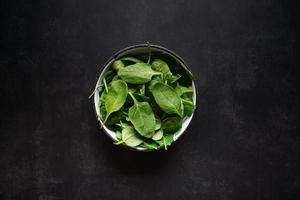 Fresh spinach leaves in bowl on rustic black table. Top view. photo