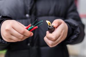 Boy lighting up several firecrackers in his hand using lighter. Kid getting ready for celebration with fireworks or pyrotechnic products . Boy holding a burning petard in his hand. Close up shot photo