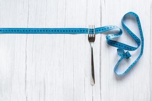 Measuring tape around fork, Weight loss concept, Top view of the background. Centimeter for measuring length and width on a white wooden background. Tailor photo