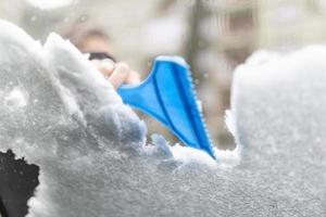 Women hand removes snow from car windshield in winter day, cleaning car from snow photo