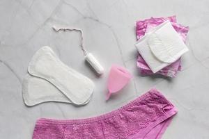 Pink pants with sanitary napkins, tampons, menstrual cup on white background. Concept of critical days, menstruation photo