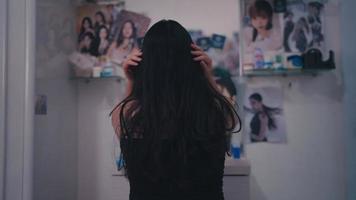 rear view of an Asian woman looking in the mirror at the dresser video