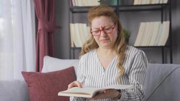 a velho mulher com óculos tem problema vendo e dela olhos ferir. maduro mulher lendo uma livro tem dolorido olhos e tem dificuldade vendo. video