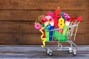 Shopping cart with items for birthday celebration on wooden background.