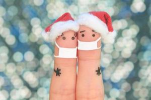 Fingers art of couple in medical mask from COVID-2019 celebrates Christmas. Concept of people in New Year hats. Toned image. photo