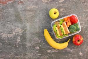 Sandwiches, fruits and vegetables in food box on old wooden background. Top view. Flat lay. photo