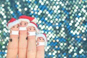 Fingers art of family in medical mask from COVID-2019 celebrates Christmas. Concept of people in New Year hats. photo