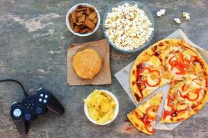 Fast food and video game controller on old wooden background. Concept of junk eating. Top view. Flat lay. photo