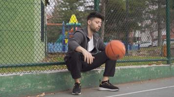 jovem homem sozinho em a basquetebol tribunal. jovem homem jogando basquetebol sozinho olhando para amigos. video