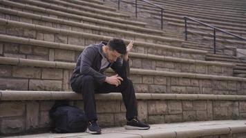 Sad lonely man sitting on the ground outdoors in the city stressed and tired. Frustrated man depressed and thoughtful. Family problems, future anxiety, separation from lover. video