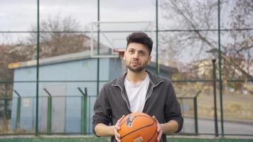 feliz jovem homem conteúdo e pacífico com vida. a jovem homem jogando basquetebol dentro a aberto ar basquetebol quadra é conteúdo e feliz com a situação ele é em. video