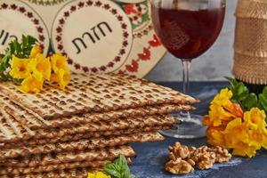 Pesach celebration concept - Jewish holiday Pesach. Background with yellow flowers with glass of wine, matzah and plate of seder on blue background. Traditional Hebrew inscriptions on plate. photo
