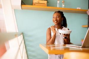 Young black woman having a healthy breakfast while working on laptop in the cafe photo