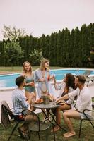 grupo de jóvenes animando con sidra junto a la piscina en el jardín foto