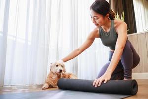 young Asia woman unrolling roll black yoga mat for playing yoga with her dog at home photo