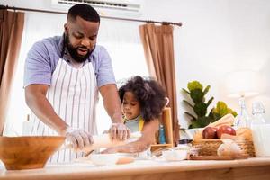 Happy African American father and daughter having fun while preparing cookie dough at home. happy family time. photo